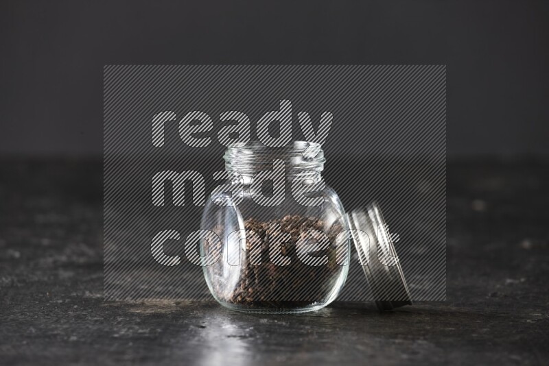 A glass spice jar full of cloves on textured black flooring
