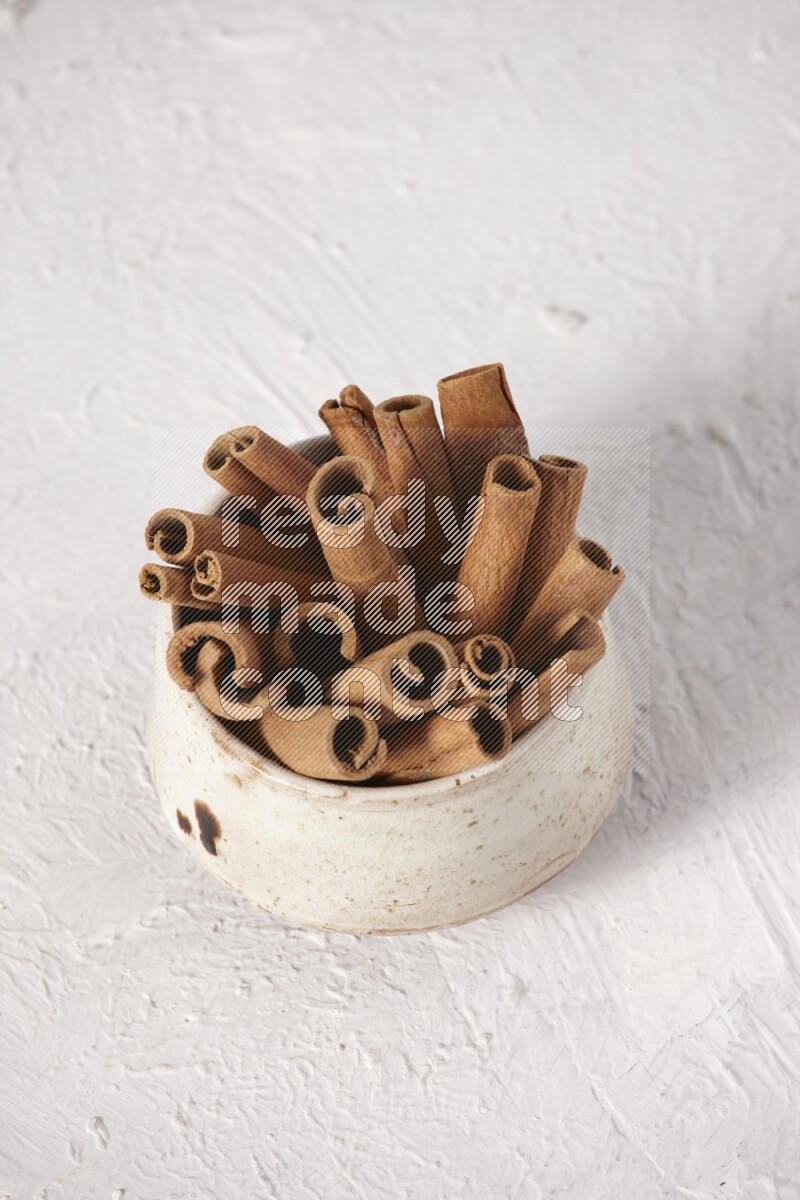 Cinnamon sticks in a beige bowl on a white background