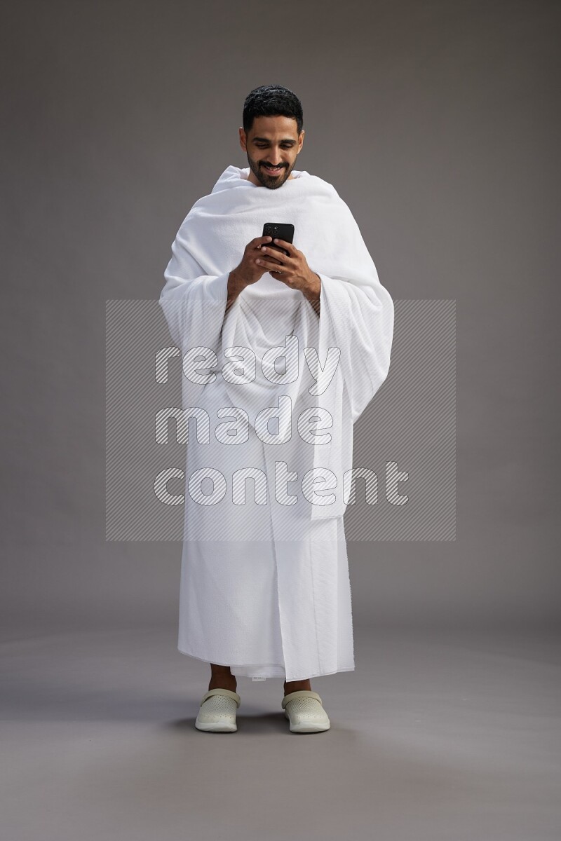 A man wearing Ehram Standing texting on phone on gray background