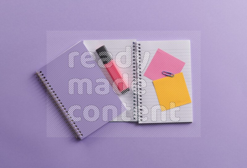 A purple notebook with different school supplies on purple background