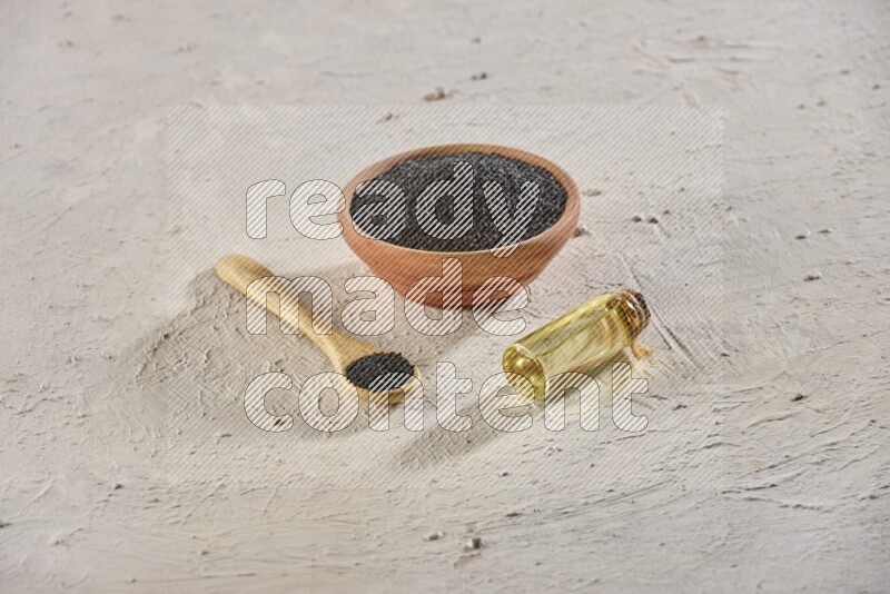 A wooden bowl and spoon full of black seeds with a bottle of black seeds oil on a textured white flooring