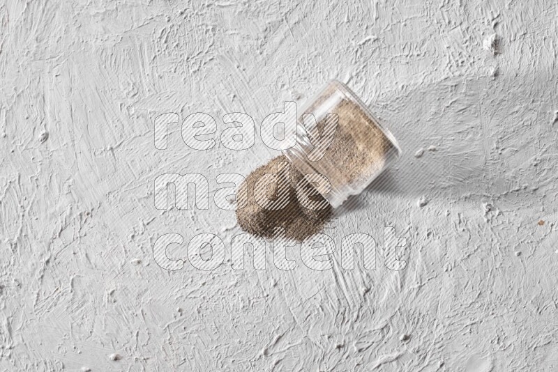 Flipped glass jar full of black pepper powder on a textured white flooring