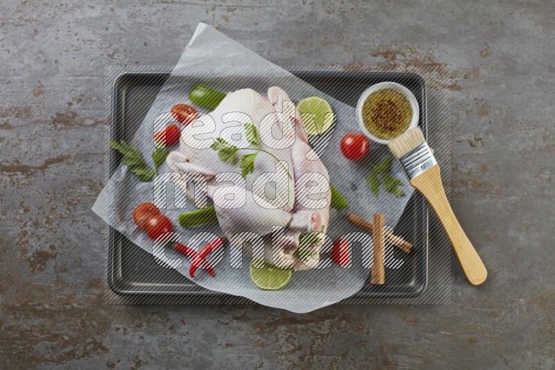 whole raw chicken on an oven trey direct on a rustic grey background