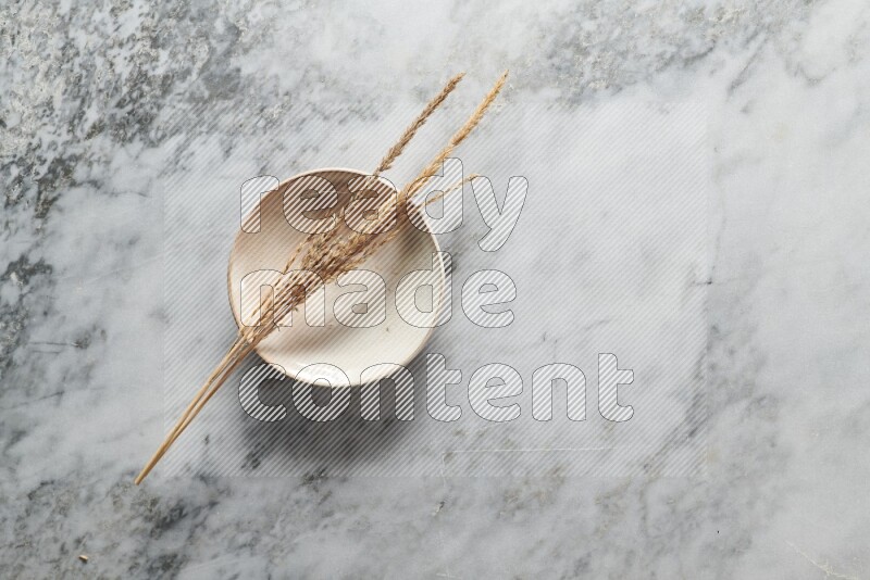 Wheat stalks on beige pottery plate on grey marble background