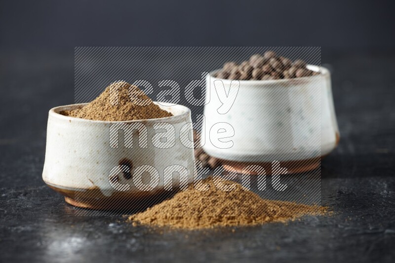 2 beige bowls, one full of allspice powder and the other full of whole balls and both spread on a textured black flooring