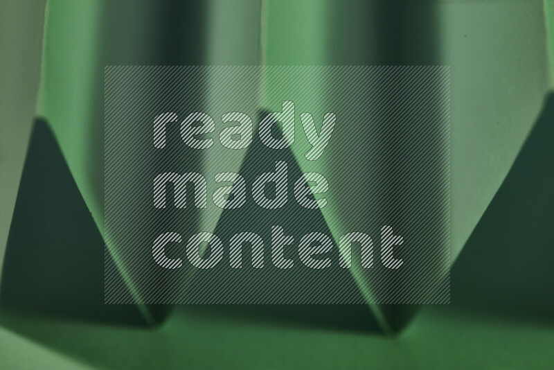 A close-up abstract image showing sharp geometric paper folds in green gradients