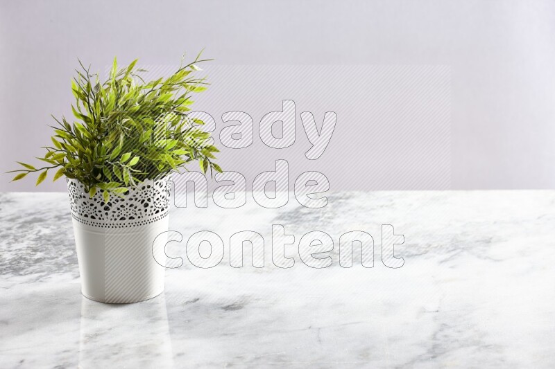 Green artificial plant in white decorative pot on grey marble background