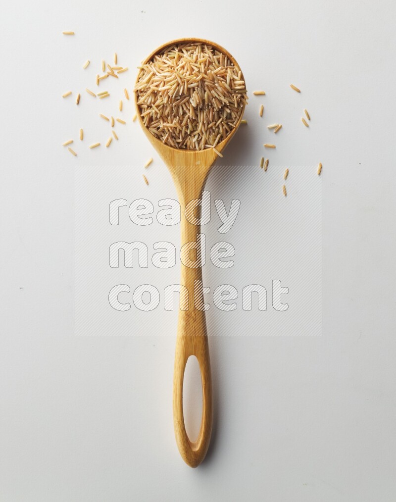 Top-view of a long grain brown rice inside a wooden spoon on white background