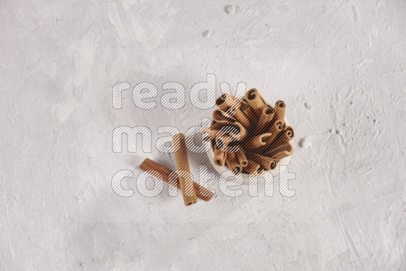 Cinnamon sticks in a beige bowl and more sticks beside it on white background