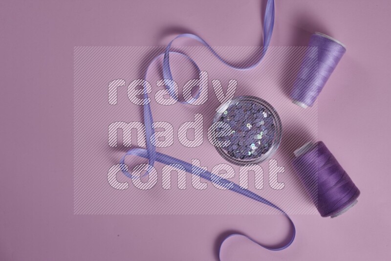 A purple and pink collection of sewing and tailoring tools arranged on a pink background