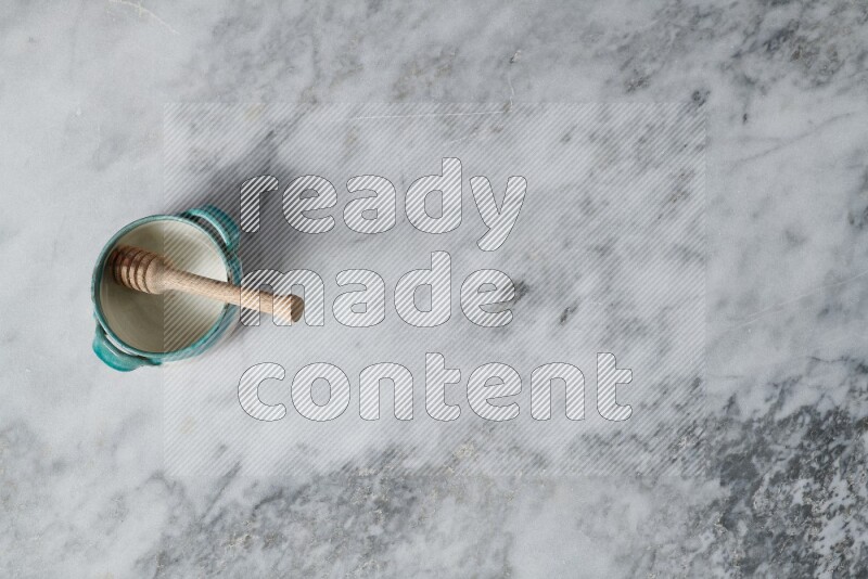 Multicolored pottery bowl with wooden honey dipper in it on grey marble background