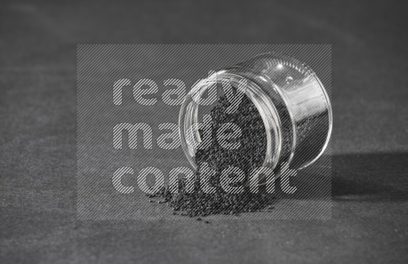 A flipped glass jar full of black seeds and the seeds spread out on a black flooring