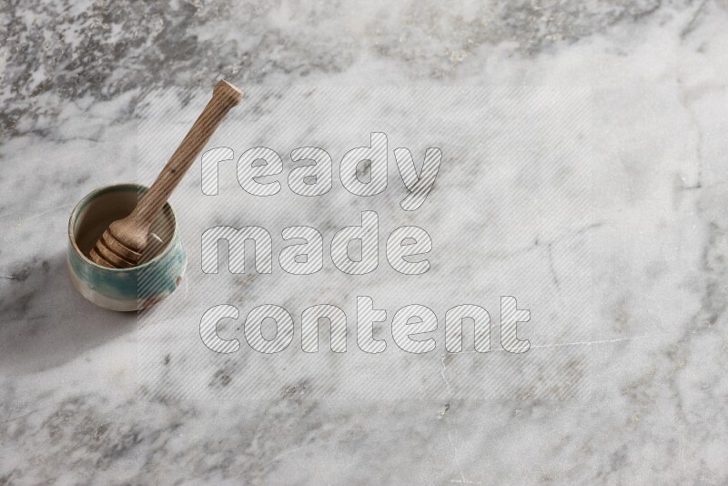 Multicolored pottery bowl with wooden honey dipper in it on grey marble background