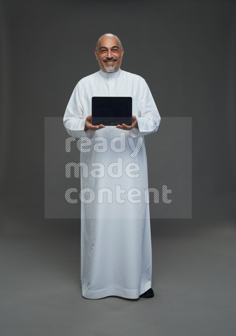 Saudi man without shomag Standing working on tablet on gray background