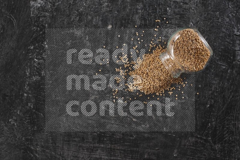 وعاء زجاجي ممتلئ ببذور الخردل والوعاء مقلوب والبذور متناثرة على أرضية سوداء