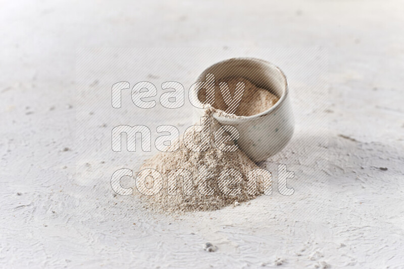 A beige pottery bowl full of onion powder with fallen powder from it on white background