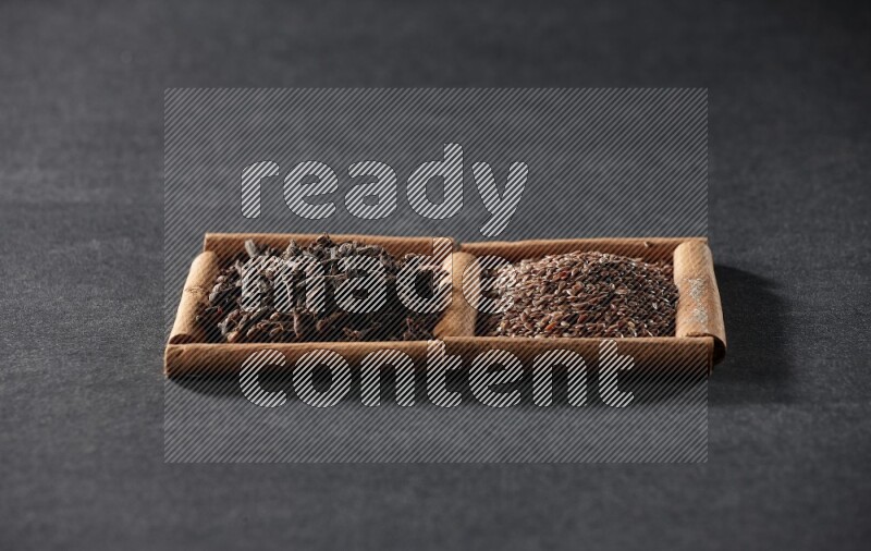 مربعان من أعواد القرفة ممتلئان ببذور الكتان والقرنفل علي خلفية سوداء