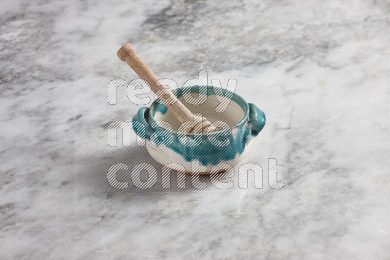 Multicolored pottery bowl with wooden honey dipper in it on grey marble background