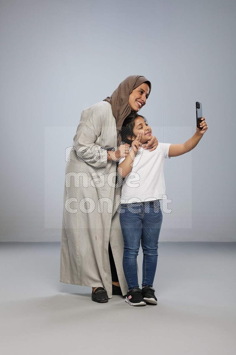 A girl standing taking selfie with her mother on gray background
