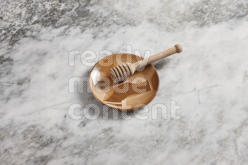Multicolored pottery plate with wooden honey dipper in it on grey marble background