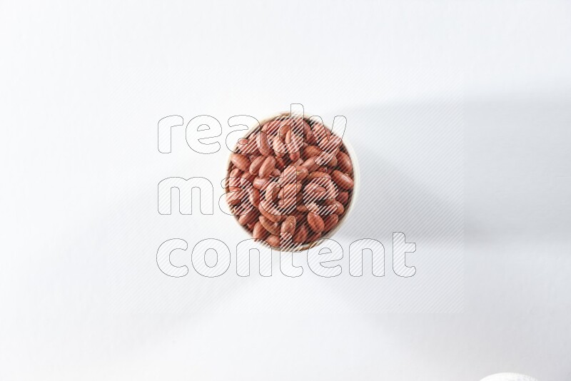A beige ceramic bowl full of red skin peanuts on a white background in different angles