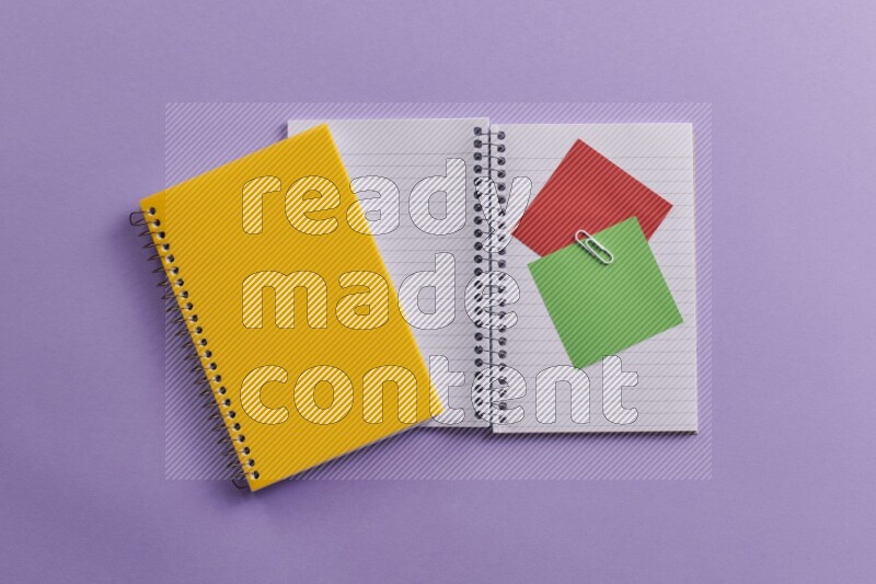 A yellow notebook with school supplies on purple background