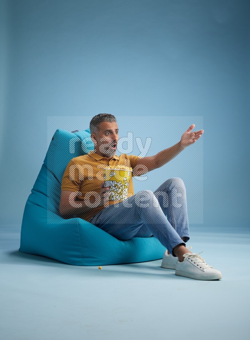 A man sitting on a blue beanbag and eating popcorn