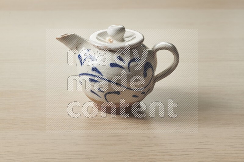 A pottery teapot on light wooden background