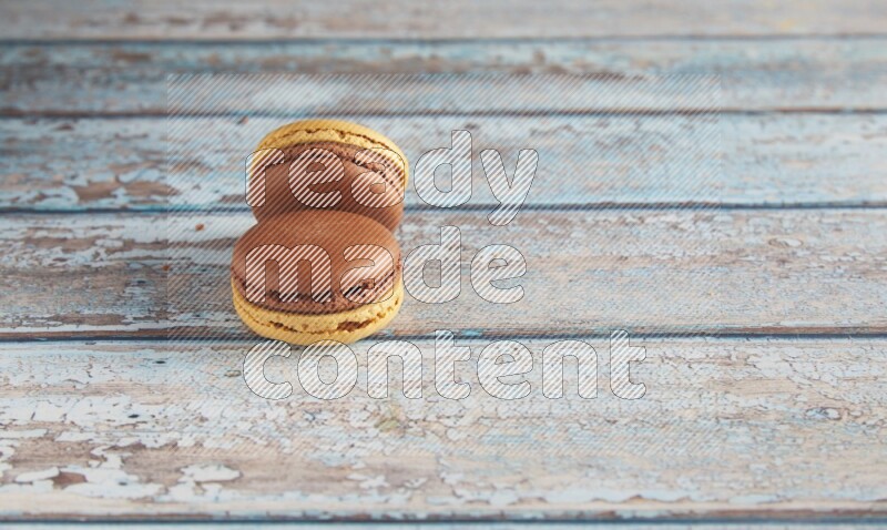 45º Shot of two Yellow and Brown Chai Latte macarons on light blue wooden background