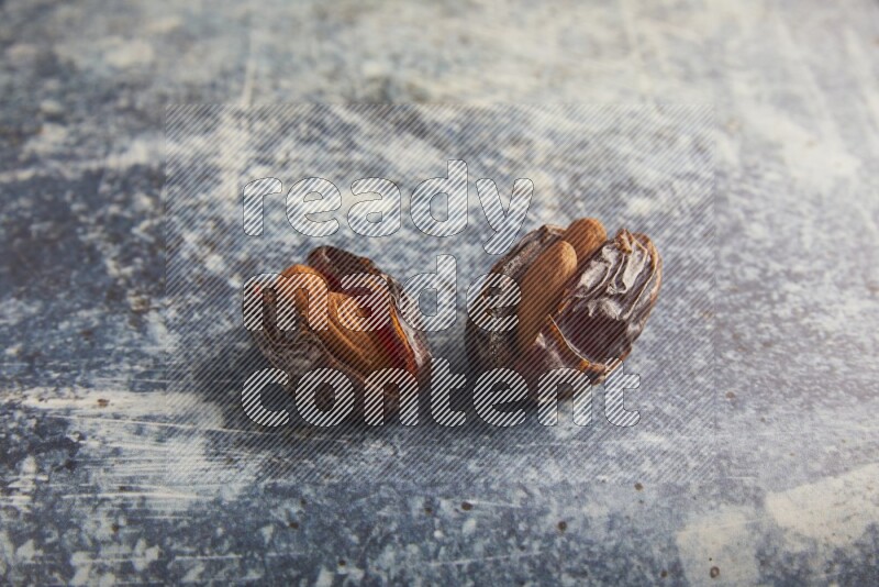 two almond stuffed madjoul dates on a rustic blue background