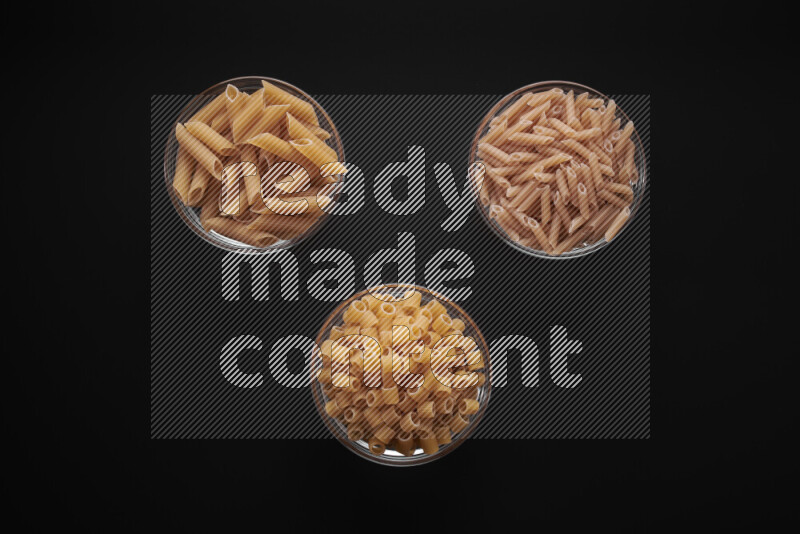 Different pasta types in glass bowls on black background
