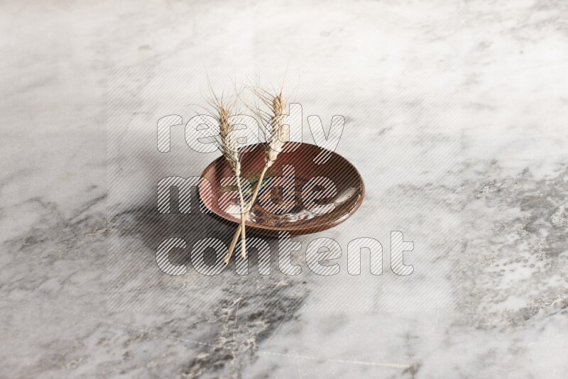 Wheat stalks on decorative pottery plate on grey marble background