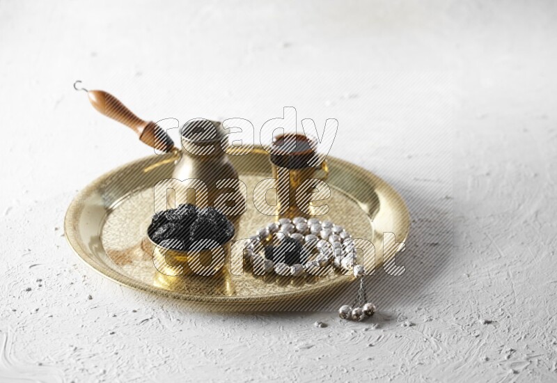 Dried plums in a metal bowl with coffee and prayer beads on a tray in a light setup