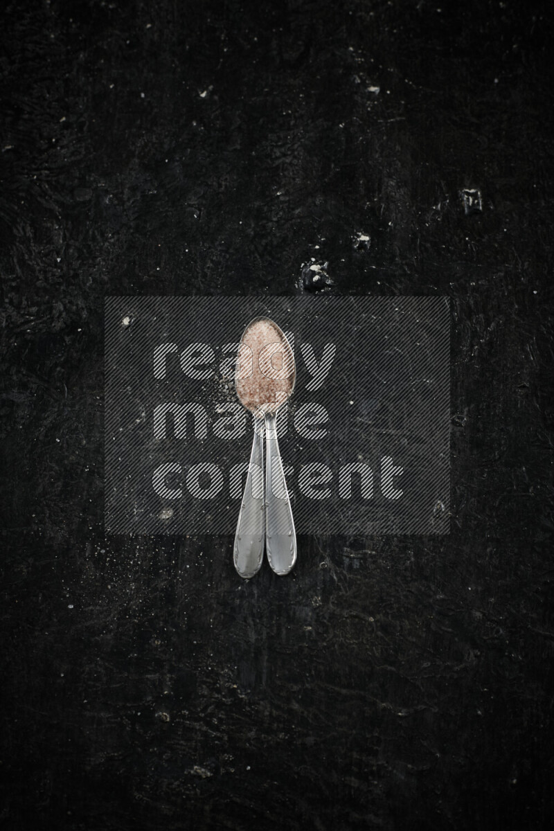 2 metal spoons filled with pink himalayan salt on black background