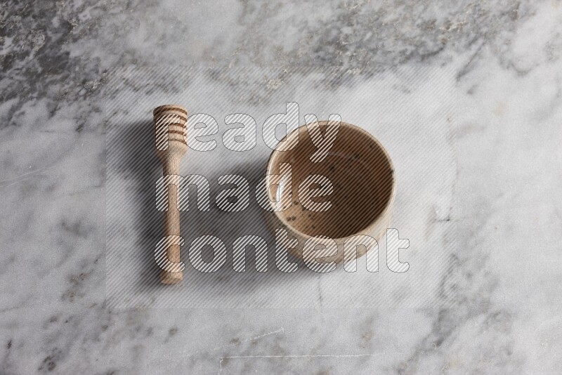 Multicolored pottery bowl with wooden honey dipper on the side on grey marble background