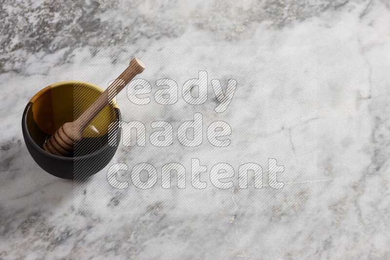 Multicolored pottery bowl with wooden honey dipper in it on grey marble background