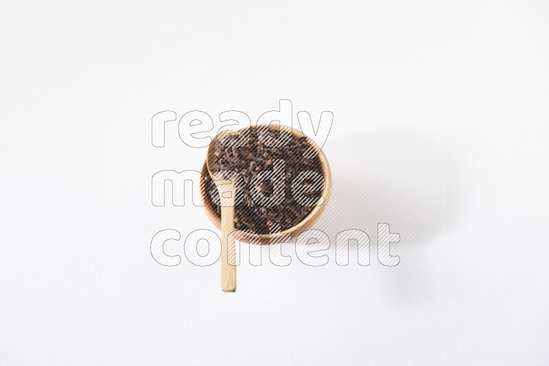 A wooden bowl and a wooden spoon full of cloves on a white flooring