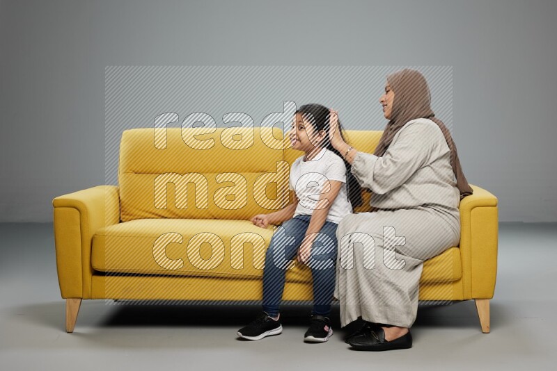 A mother sitting styling hair for her daughter on gray background