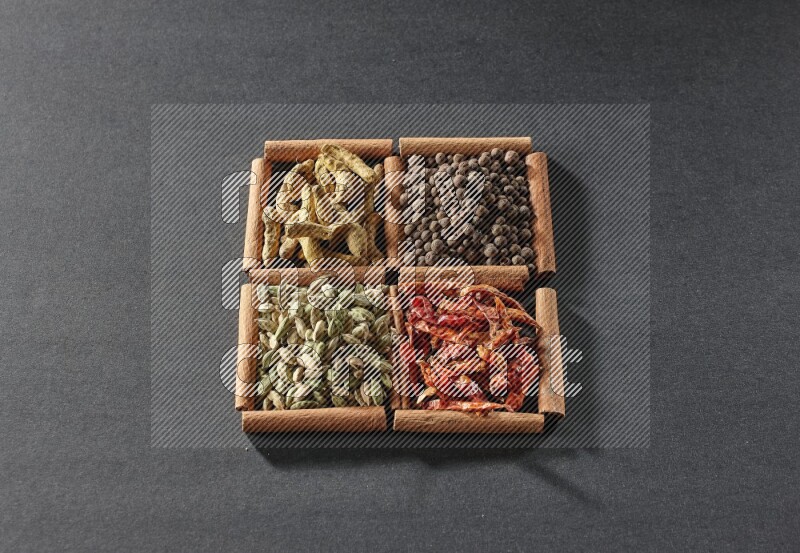 4 مربعات من عيدان القرفة ممتلئة بحبوب الهيل والفلفل الحار وبهار الفلفل الحلو وأصابع الكركم على أرضية سوداء