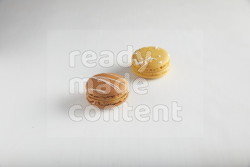 45º Shot of of two assorted Brown Irish Cream, and Yellow Piña Colada macarons on white background