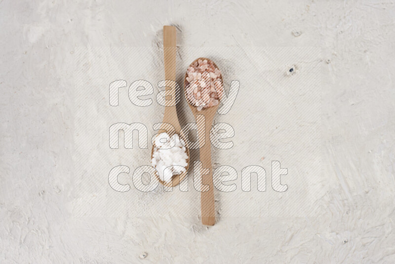 2 wooden spoons filled with fine and coarse salt on white background