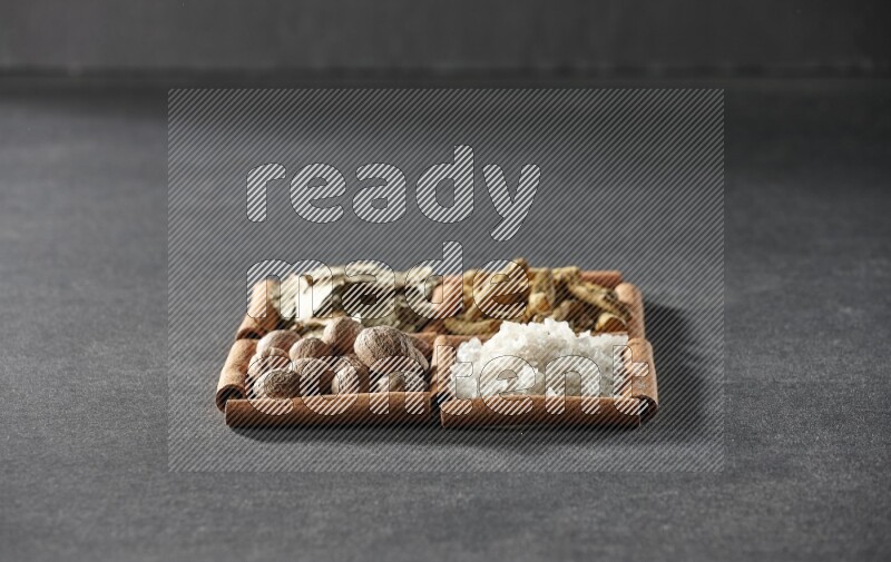 4 مربعات من عيدان القرفة ممتلئة بأوراق الغار والملح الأبيض وأصابع الكركم وجوزة الطيب على أرضية سوداء