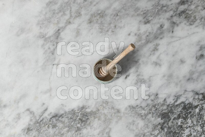 Multicolored pottery bowl with wooden honey dipper in it on grey marble background