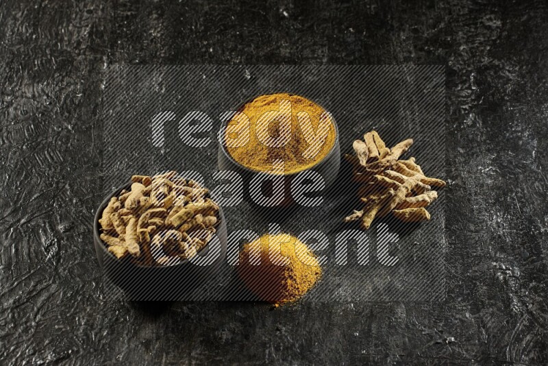 وعاءان من الفخار باللون الأسود، أحدهما ممتلئ ببودرة الكركم والآخر ممتلئ بأصابع كاملة من الكركم المجفف على خلفية سوداء