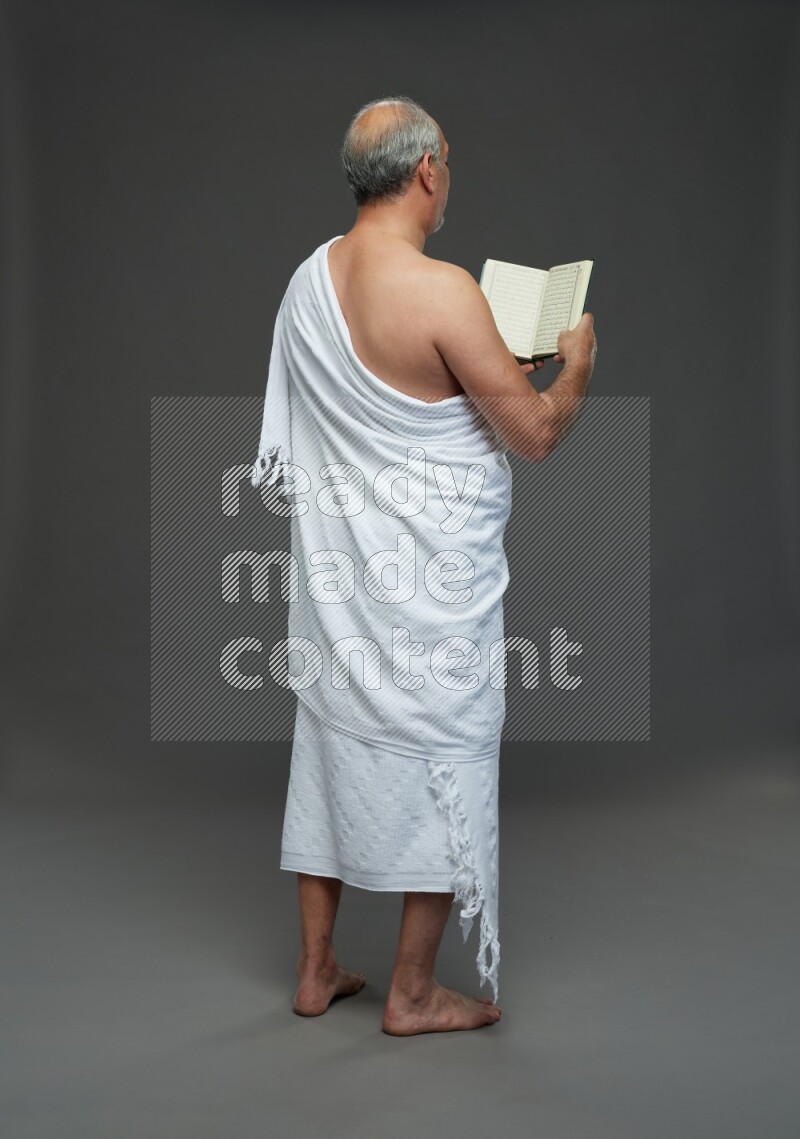 A man wearing Ehram Standing reading quran on gray background