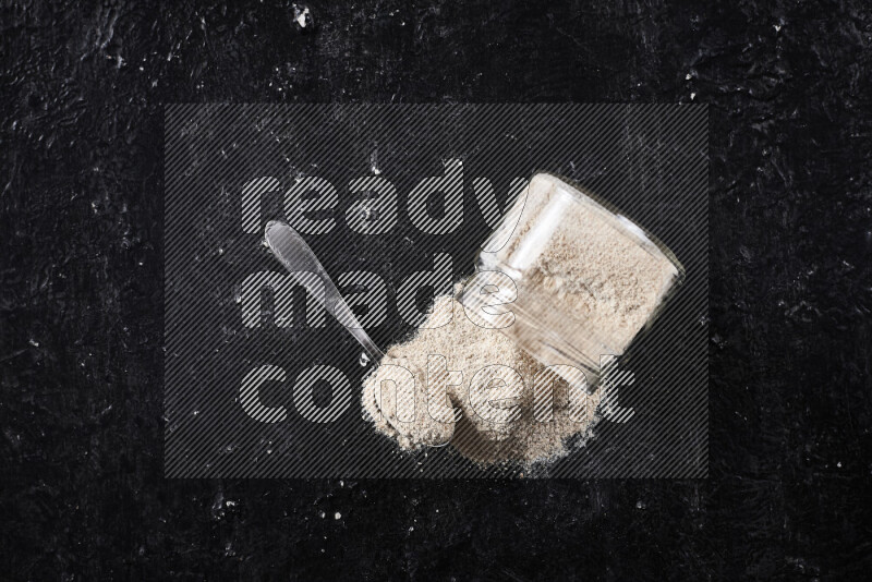 A glass jar full of onion powder flipped with some spilling powder on black background