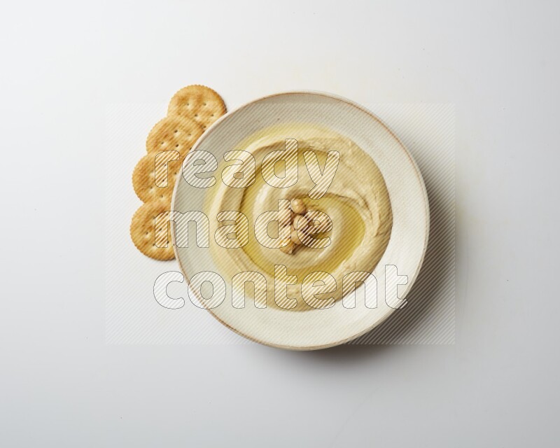 Hummus in a pottry plate garnished with roasted chickpeas on a white background