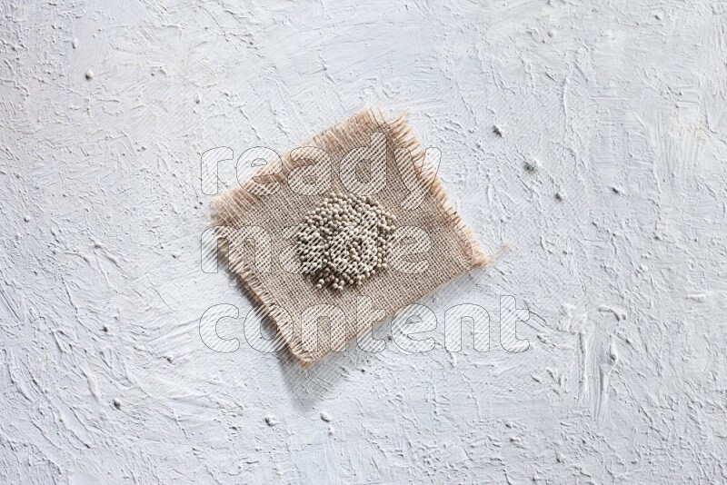 White pepper beads on a burlap piece of fabric on textured white flooring