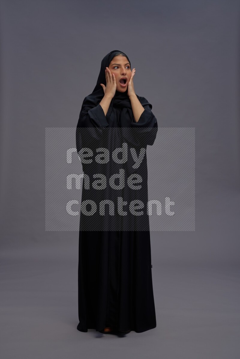 Saudi woman wearing Abaya standing hands behind head on gray background