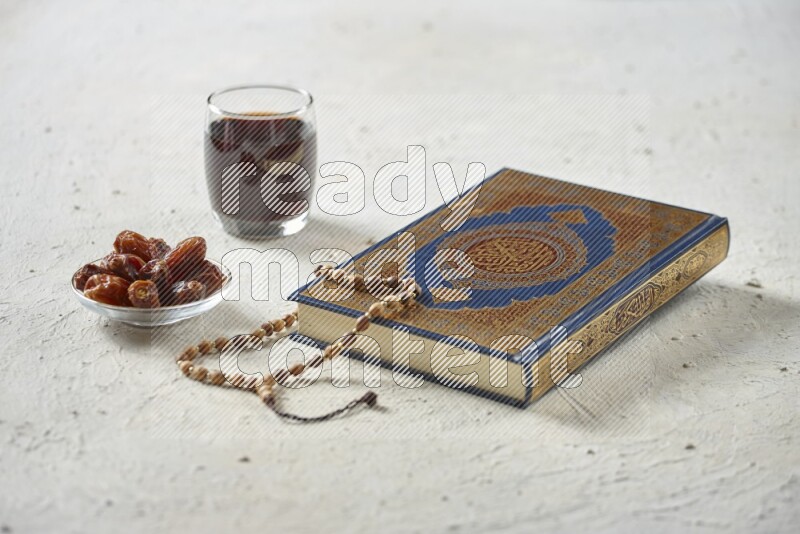 Quran with dates, prayer beads and different drinks all placed on textured white background